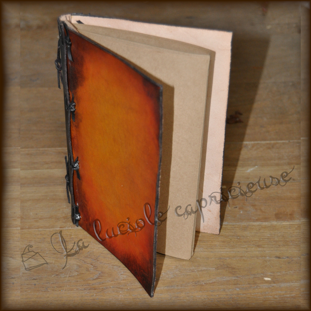 Vue de haut d'un petit cahier en cuir de bovin tanné végétal, teinté dégradé orange rouge acajou, papier kraft