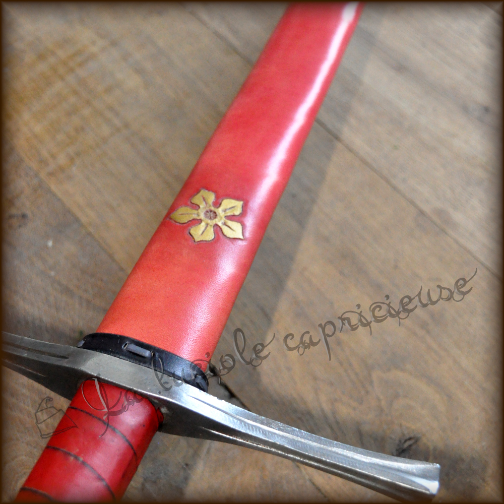 Vue détaillée d'un fourreau d'épée médiéval en cuir de bovin tanné végétal, motif en relief quintefeuille, teinté jaune sur fond rouge