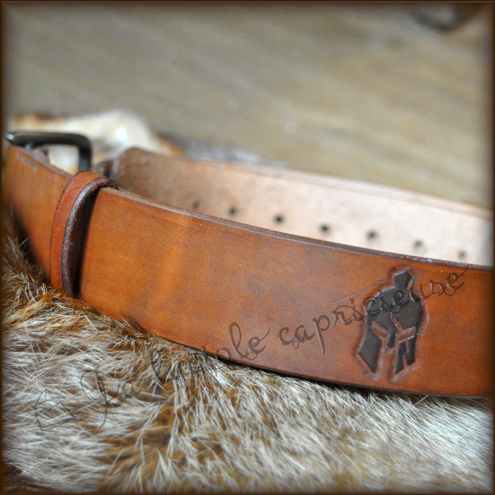 Vue détaille d'une ceinture faite main en cuir de bovin tanné végétal, motif en relief casque, noir sur fond marron