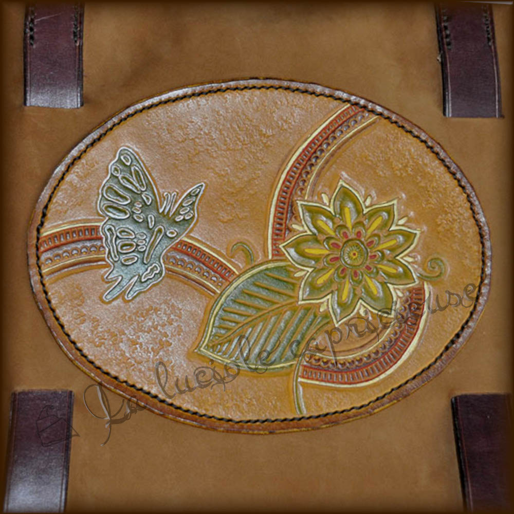 Médaillon décoratif en cuir de bovin tanné végétal, cousu main, motif en relief papillon et fleur, teinté en couleurs sur fond orangé